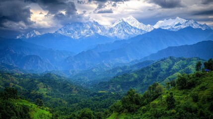 Fototapeta premium Panoramic view of snow capped mountains under a dramatic sky, layered hills covered in lush green vegetation in the foreground. 
