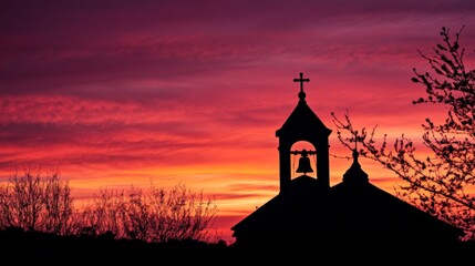 Fototapeta premium Silhouette of church bell tower against vibrant sunset sky