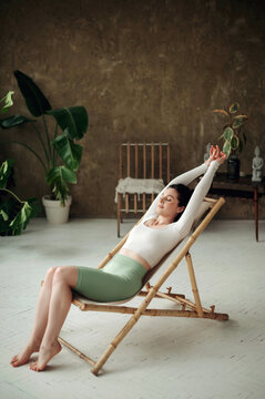 Beautiful young woman sitting on a sunbad chair in a room and relaxing