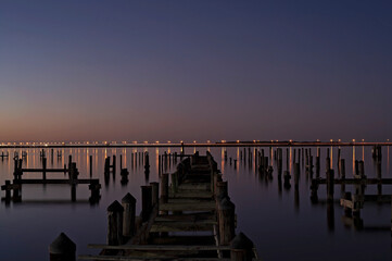 Abandoned wooden pier at twilight with reflections on calm water