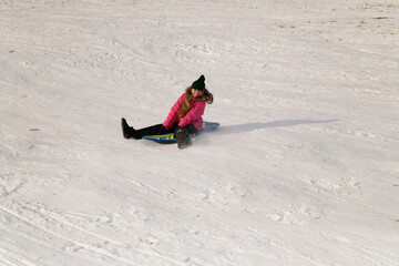 Happy little girl spinning on sled down snow covered hill