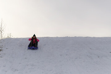 Looking up at young girl sledding down snowy hill