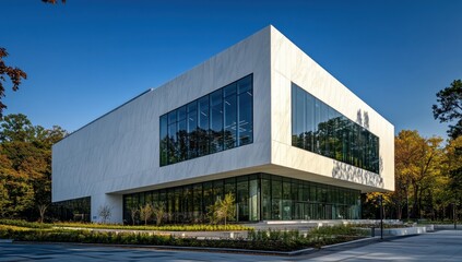 Fototapeta premium Modern white marble building with large glass windows, situated in a landscaped area with trees.