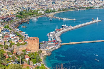 Aerial view of the Red Tower and the harbor in Alanya, Turkey. Medieval tower stands next to the bustling marina, surrounded by vibrant city buildings and turquoise waters of the Mediterranean Sea