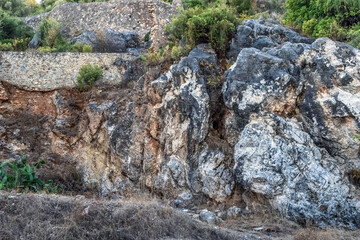 A rocky hillside with exposed layers of stone near the walls of Alanya Castle in Turkey. The natural textures of the rock contrast with the greenery and the historic stone walls in the background