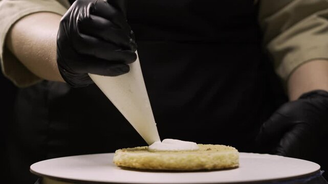 step by step process of making benta cake with banana filling. Pastry chef carefully squeezes cream cheese from a pastry bag onto the first layer of cake on a stand. step three