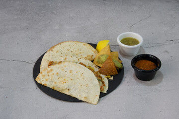 A plate of three tacos with a side of chips and a small cup of salsa