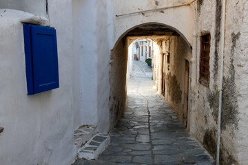 Obraz premium Narrow alley with tunnel and with whitewashed walls and stone pavement leading to a courtyard in the Greek Islands, Greece
