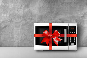 Household appliances - White Microwave gift tied red bow concrete wall background
