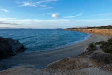 Sun shining over a secluded beach with vegetation and cliffs at sunset