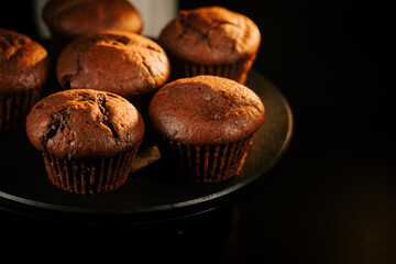 Freshly baked chocolate muffins on a round black platter in a dimly lit kitchen setting
