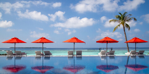 Red parasols and sun loungers next to a swimming pool at a beach resort