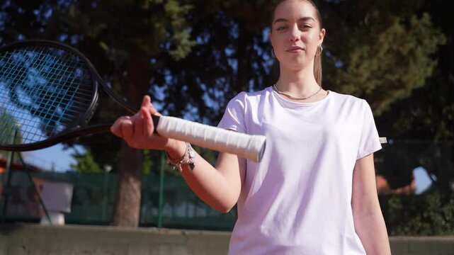 A teenage tennis player warming his wrist before a tennis workout or a competition, looking at the camera and smiling.