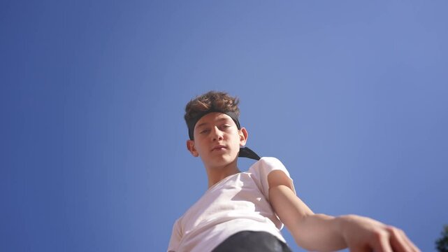 Low-angle shot of a teenage male tennis player serving on a clay court.