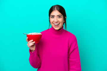 Young caucasian woman holding a bowl of cereals isolated on blue background with surprise and...