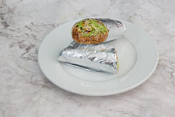 A silver foil wrapped burrito sits on a white plate