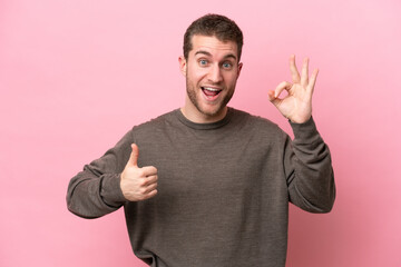 Fototapeta premium Young caucasian man isolated on pink background showing ok sign and thumb up gesture