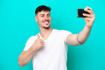 Young caucasian handsome man isolated on blue background making a selfie with mobile phone