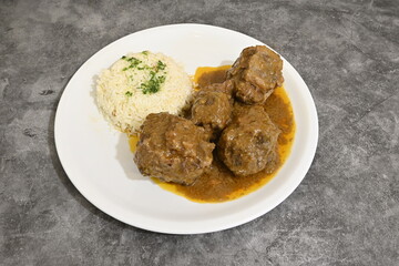 A plate of meatballs and rice with a sauce on top