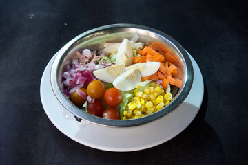 A bowl of salad with a variety of vegetables including tomatoes, corn