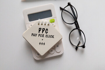 A note labeled Pay Per Click resting on a calculator set on the desk, symbolizing online...