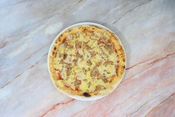 A pizza with yellow cheese and meat toppings sits on a marble countertop