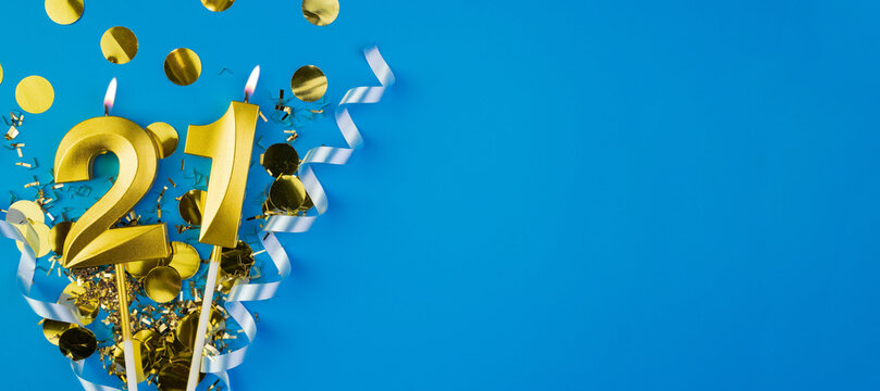 Celebrating 21 years. Golden burning candle in form of number twenty one on celebration festive blue background lying in sparkles. Holiday banner with copy space.