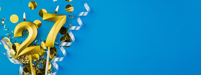 Celebrating 27 years. Golden burning candle in form of number twenty seven on celebration festive blue background lying in sparkles. Holiday banner with copy space.