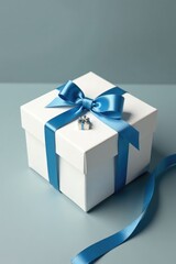 Small white gift box tied with thin blue ribbon and adorned with a small silver bow, blue ribbon, small gift, present