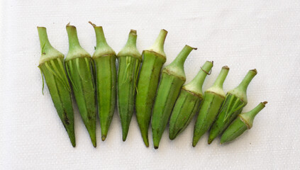 Fresh green okra pods arranged on a white cloth background.