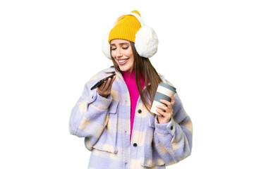 Young woman wearing winter muffs over isolated chroma key background holding coffee to take away and a mobile