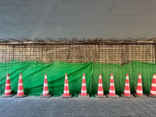 Construction is underway for the reconstruction of the tunnel under the road, on which work is being carried out. Orange traffic cones and tarp over construction wall