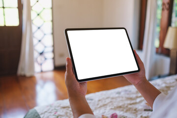 Mockup image of a woman holding tablet with blank desktop white screen on the bed at home