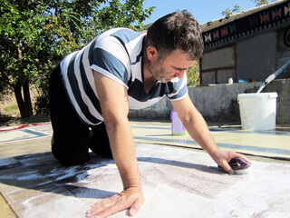 A man in the village washes the carpet with a brush