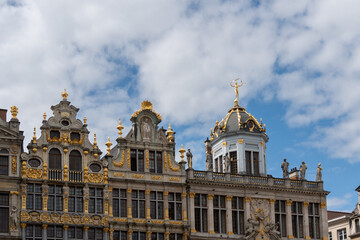 Fototapeta premium Ornate facades of historic guildhalls showcasing gilded details under a partly cloudy sky in brussels' grand place
