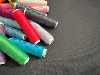 Colorful sewing thread spools on a dark fabric background with copy text space