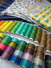 Colorful sewing thread spools and bobbins in a box and colorful fabric
