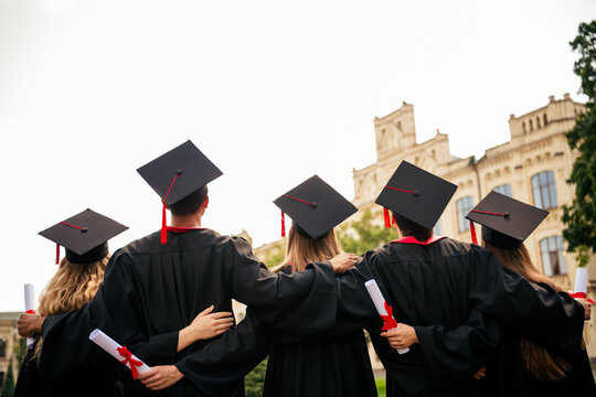 Rear photo of group students groupmates hold diploma cuddle mortarboard graduate university building outdoors