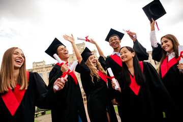 Lively group of diverse graduates celebrating in academic gowns and wearing mortarboards with joy...