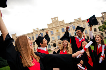 Young happy graduates celebrating outdoors on a sunny day, wearing caps and gowns. A joyful group...