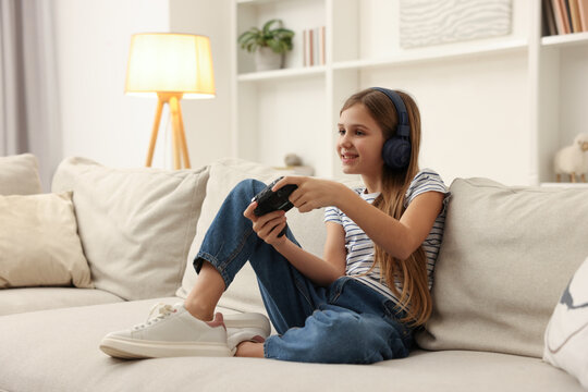Cute girl in headphones playing video game on sofa at home
