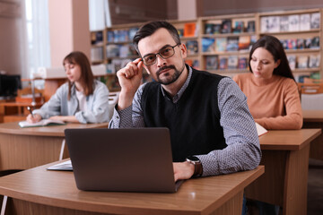 Portrait of man with laptop at desk in public library