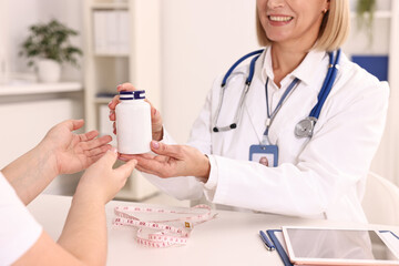 Weight loss. Smiling nutritionist giving medical bottle with pills to patient at table in clinic,...
