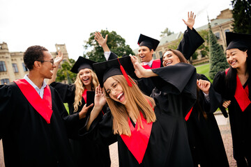 Joyful college graduates celebrating together outdoors on a vibrant summer day, expressing...