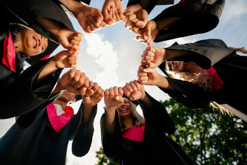 Low angle view portrait of group students arms touch make circle mortarboard gown graduation...