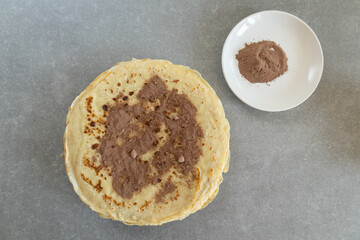 A crepe sprinkled with cocoa powder on a plate, top view.