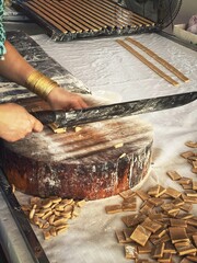  An unrecognizable person cutting candy strips into squares with a huge knife. Thoi Son island, Vietnam. Coconut candy factory. 