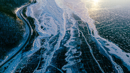 Aerial view of a road running alongside the frozen Lake Baikal at sunset, showcasing icy textures and warm golden hues.