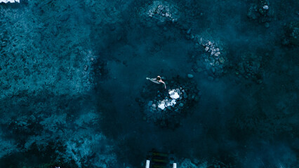 Aerial view of a lone woman relaxing in a stunning thermal spring surrounded by snowy landscapes in...