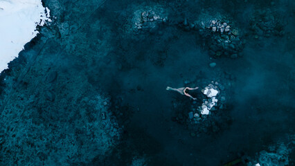 Aerial view of a lone woman relaxing in a stunning thermal spring surrounded by snowy landscapes in...